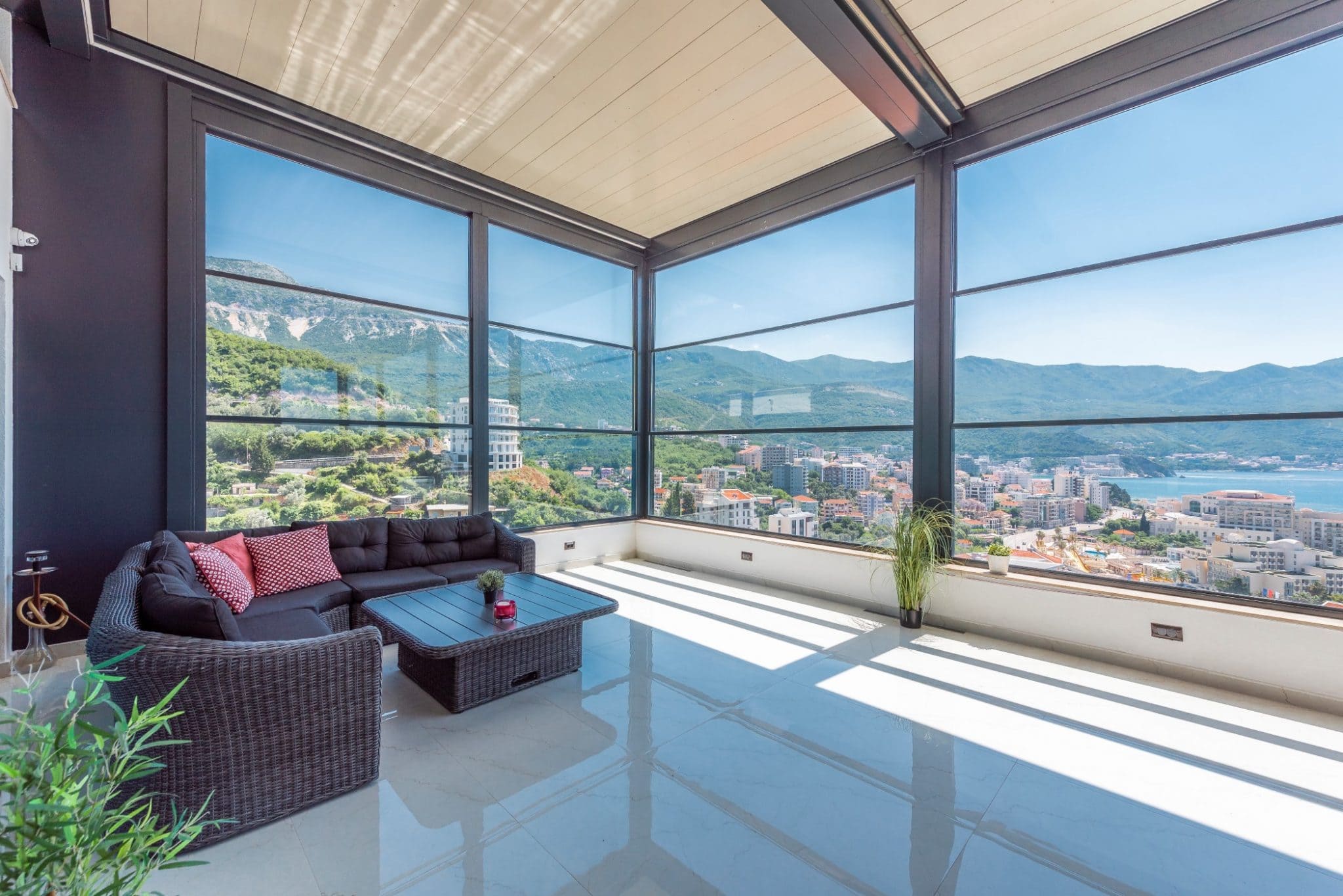 Panoramic penthouse terrace in Bečići, Montenegro: wicker furniture, floor-to-ceiling windows, and views of the sea and mountains.