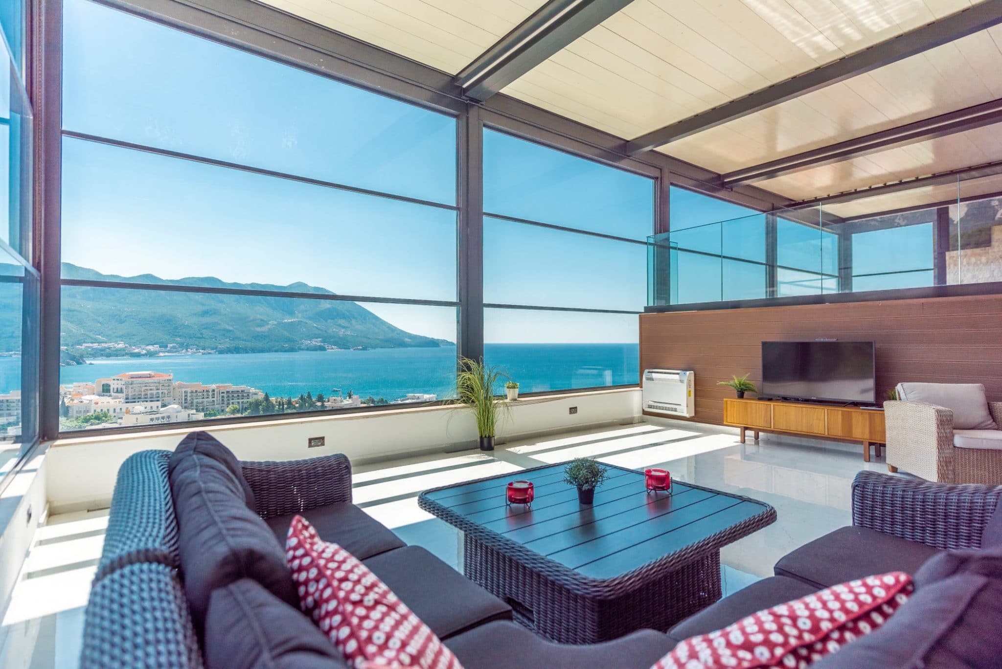Living room in a penthouse in Bečići, Montenegro: panoramic windows, sea view, wicker furniture, and a terrace.