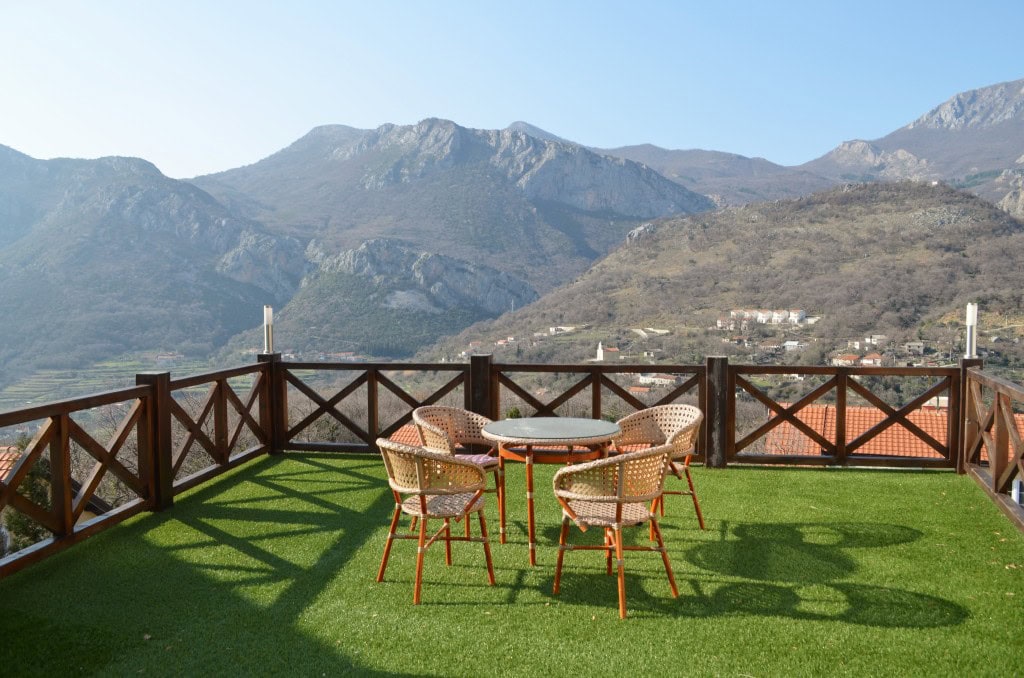 Terrace with wicker furniture and mountain views in an apartment, Bar, Montenegro. Green floor covering, wooden railing.