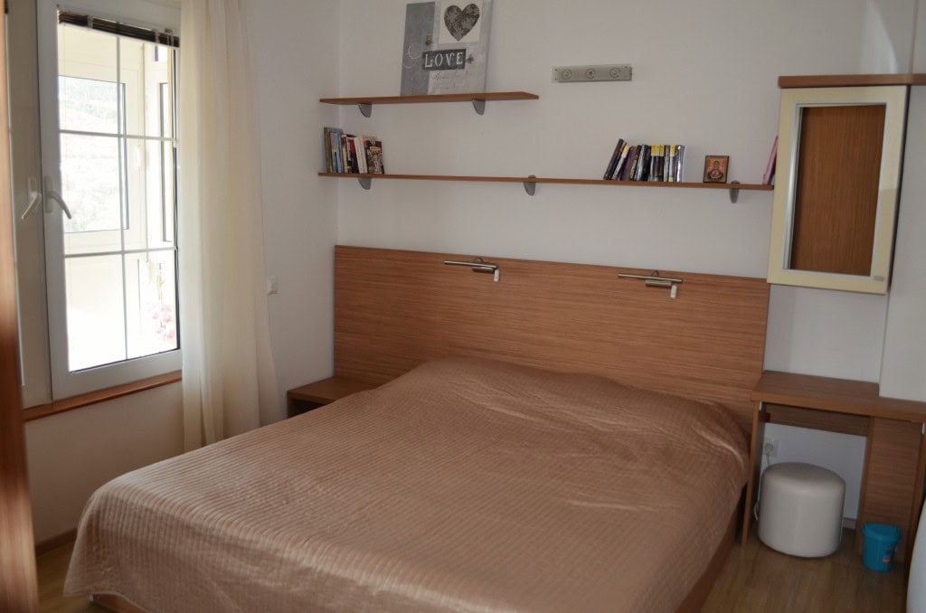 Cozy bedroom with a double bed in an apartment, Bar, Montenegro: bright interior, shelves, and a view from the window.