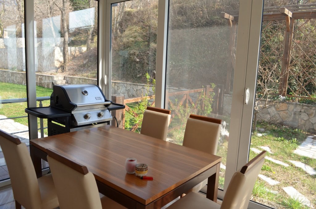 Dining area with a grill in the living room of an apartment in Bar, Montenegro, with panoramic windows and a garden view.