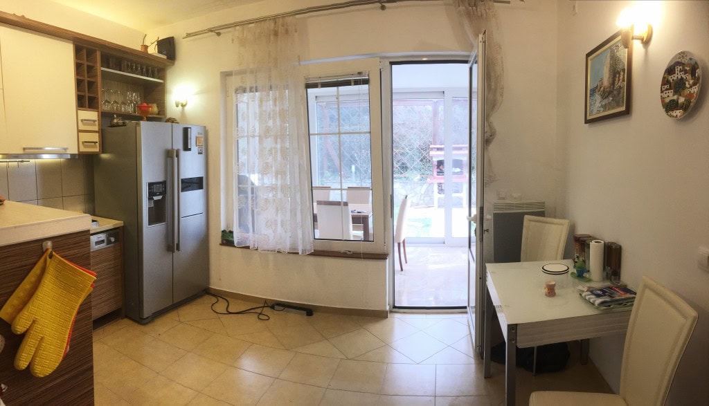 Kitchen with dining area in an apartment in Bar, Montenegro: light-colored furniture, access to the terrace, and garden view.