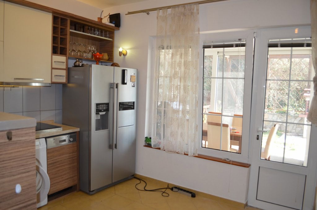 Kitchen in an apartment in Bar, Montenegro: light-colored furniture, a large refrigerator, and access to the terrace.