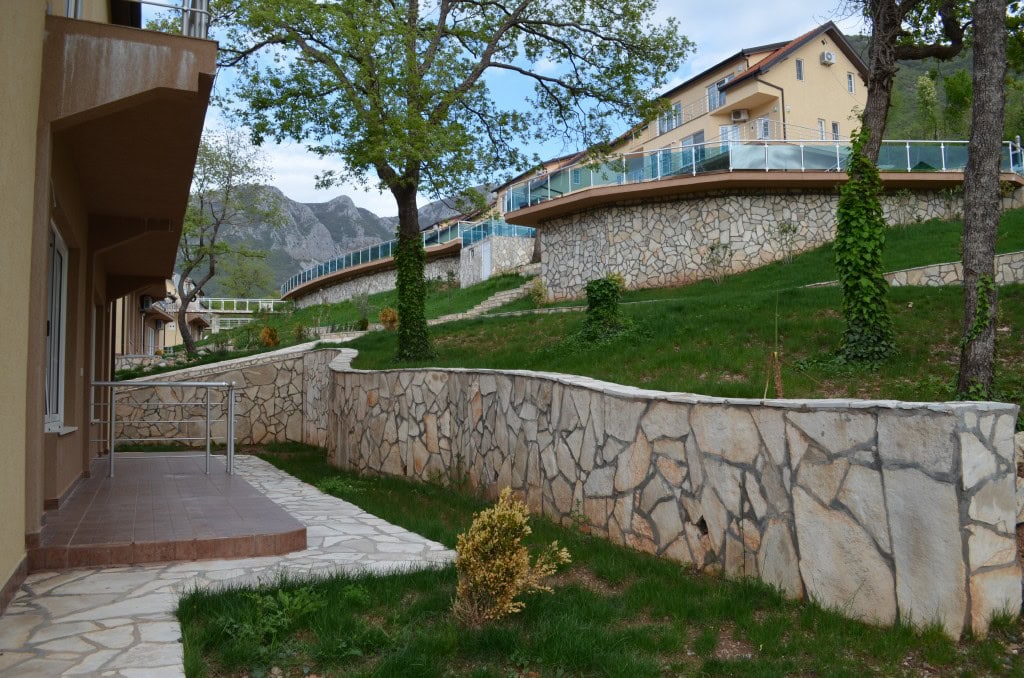 Residential complex grounds in Bar, Montenegro: stone retaining walls, terraces with railings, and mountain views.