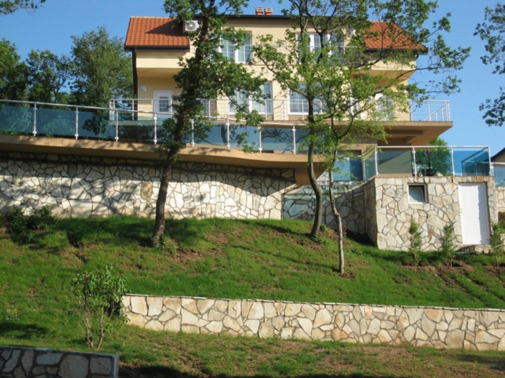 Two-story house in Bar, Montenegro: facade with stone cladding, terraces, and glass railings.