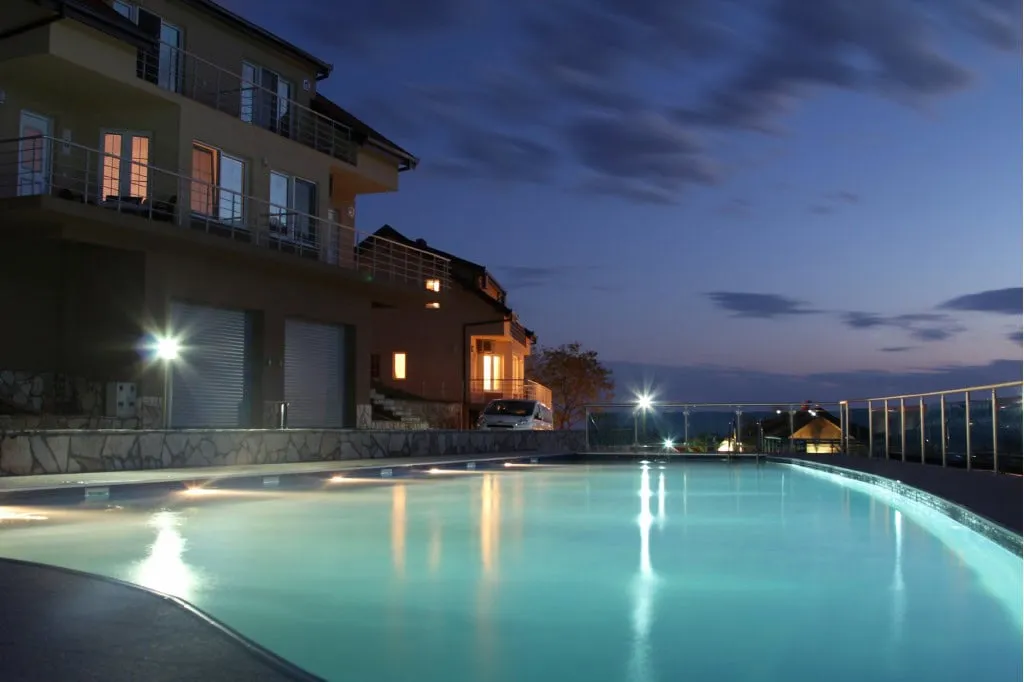 Outdoor swimming pool with underwater lights at dusk next to a residential building.