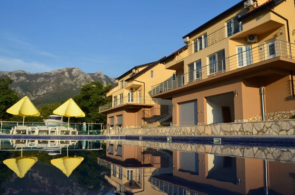 Outdoor pool with yellow umbrellas reflecting the building against mountains.