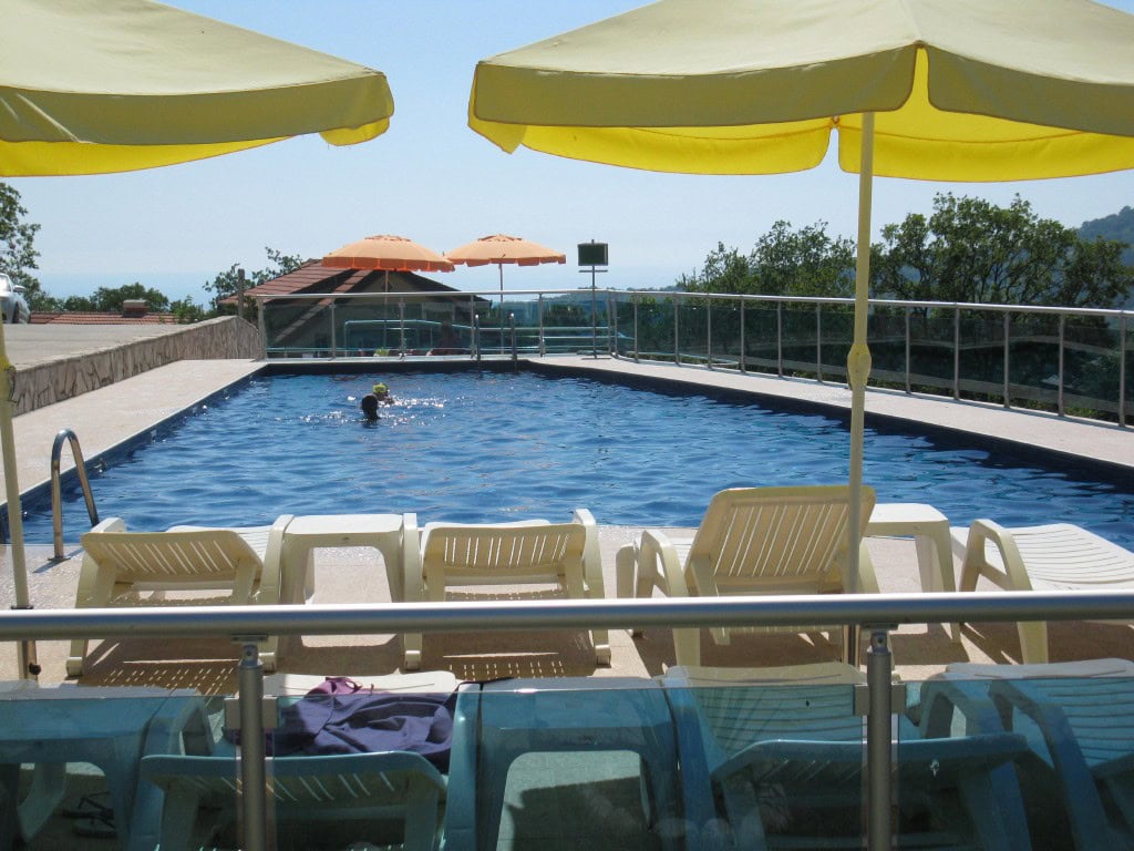 Outdoor swimming pool with sun loungers and yellow umbrellas in a residential complex, Bar, Montenegro, sea and mountain views.