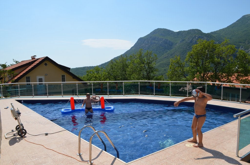 Outdoor pool with mountain views at apartments in Bar, Montenegro: a relaxation area with a terrace and fencing.