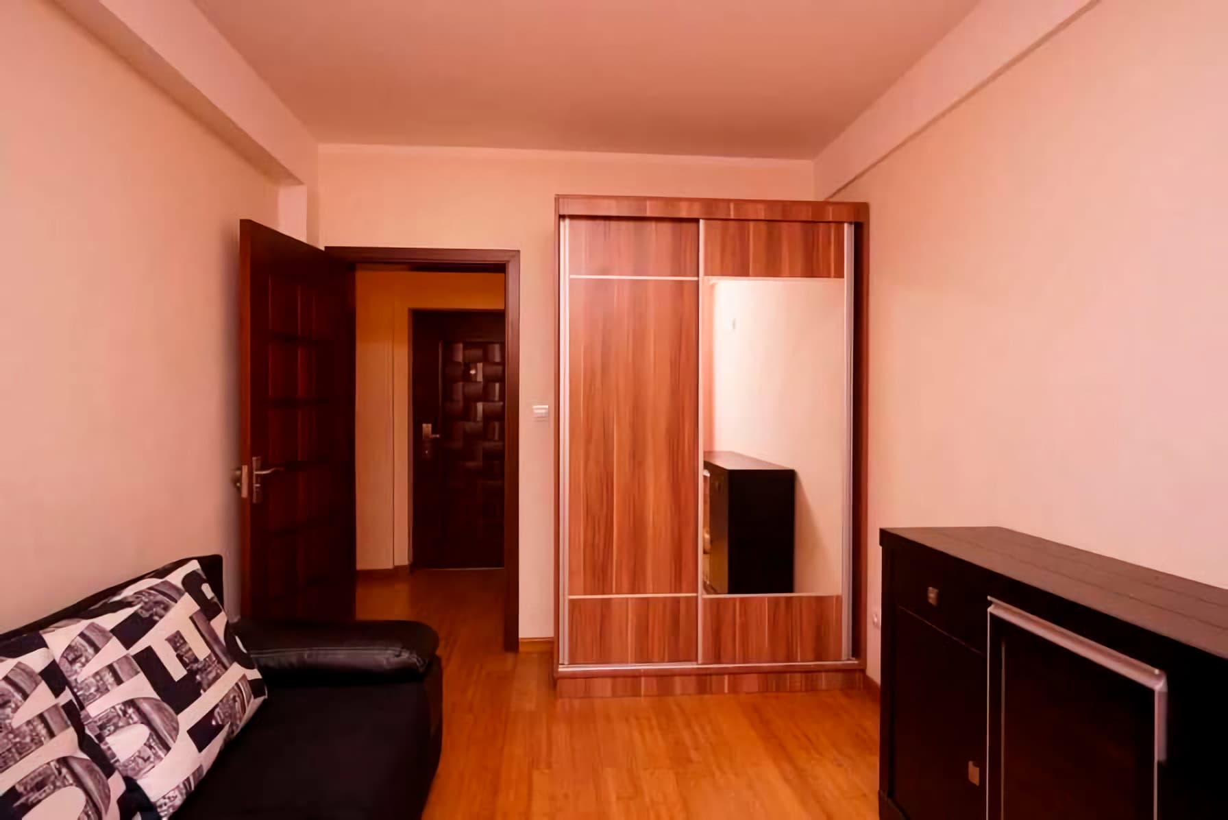 Living room in an apartment in Budva, Montenegro: a mirrored sliding wardrobe, a dark sofa, and wooden interior doors.