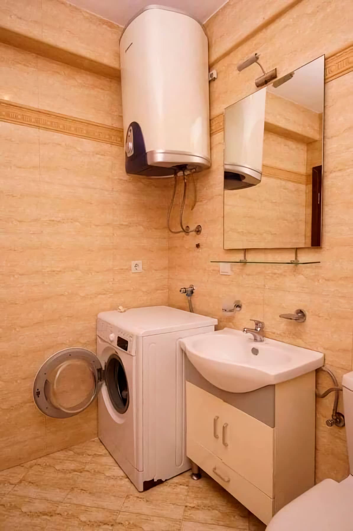 Bathroom in an apartment in Budva, Montenegro: beige tiles, washing machine, sink with vanity, and water heater.