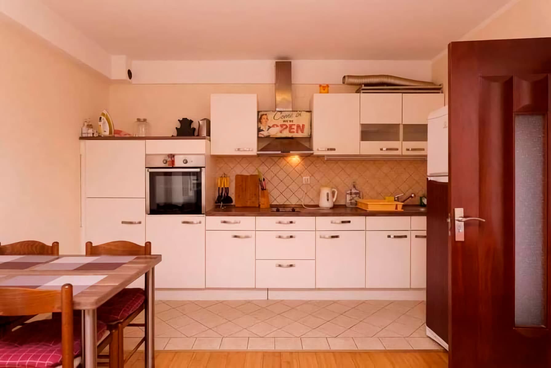Bright kitchen with white cabinetry and a dining area in an apartment in Budva, Montenegro. Cozy interior with tiled flooring.