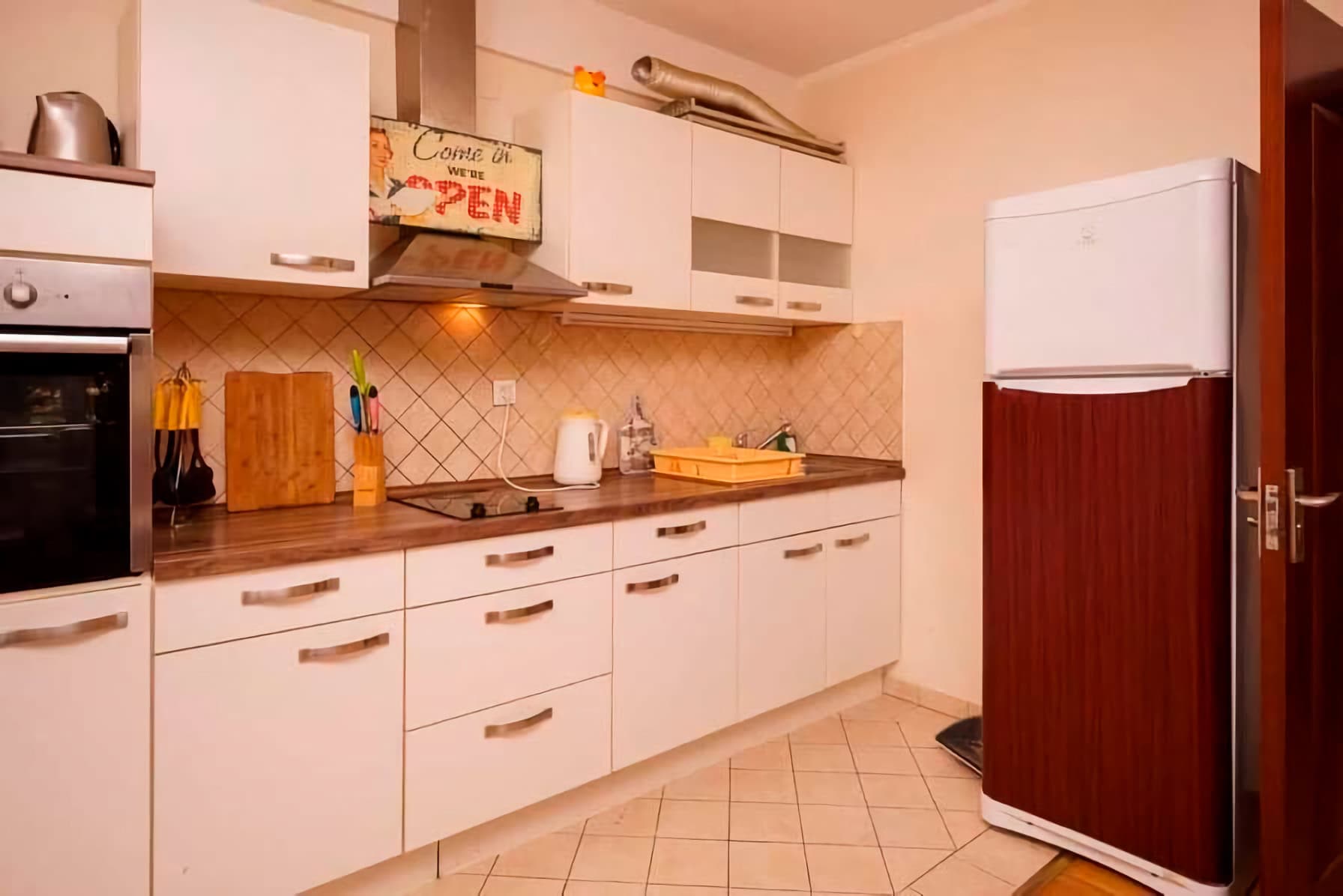 Bright kitchen in an apartment in Budva, Montenegro: white cabinets, built-in appliances, tiled backsplash, and a refrigerator.
