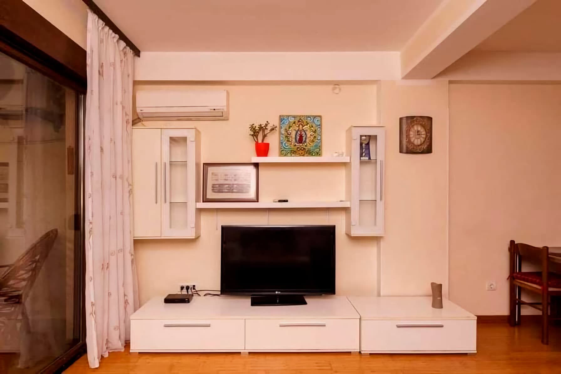 Living room with white furniture, TV area, and air conditioning in an apartment in Budva, Montenegro. Bright interior with parquet flooring.