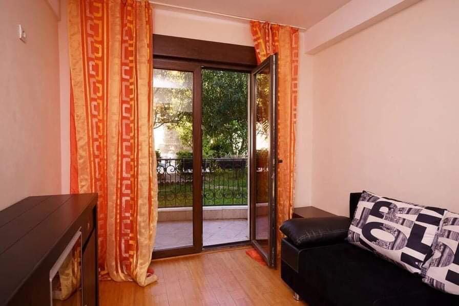Living room in an apartment in Budva, Montenegro: black sofa, parquet floor, access to a balcony overlooking a green garden.