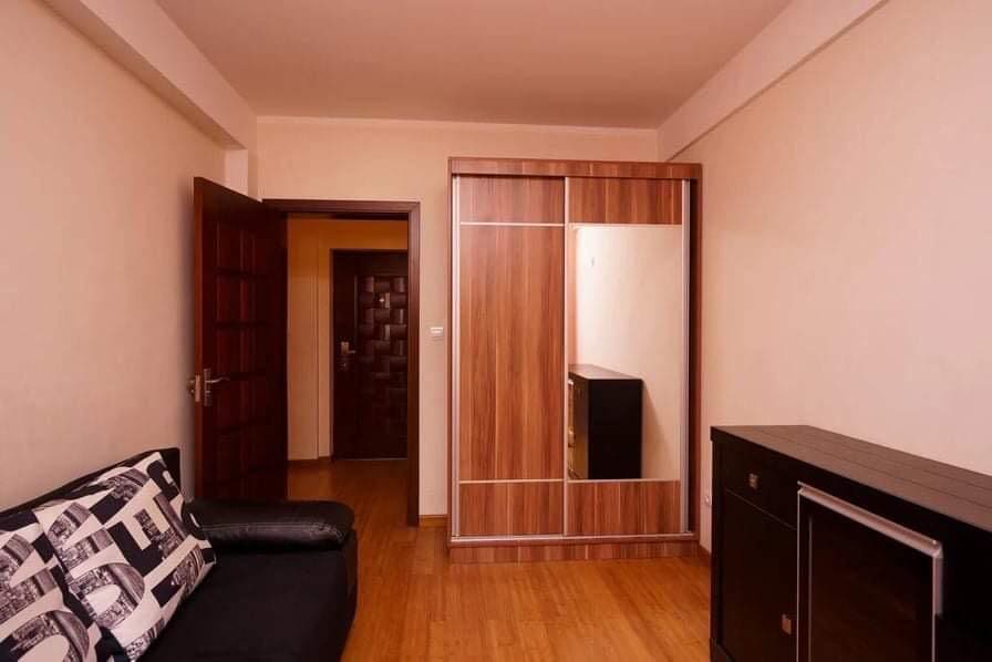 Living room in an apartment in Budva, Montenegro: a mirrored sliding wardrobe, a dark sofa, and parquet flooring in the interior.