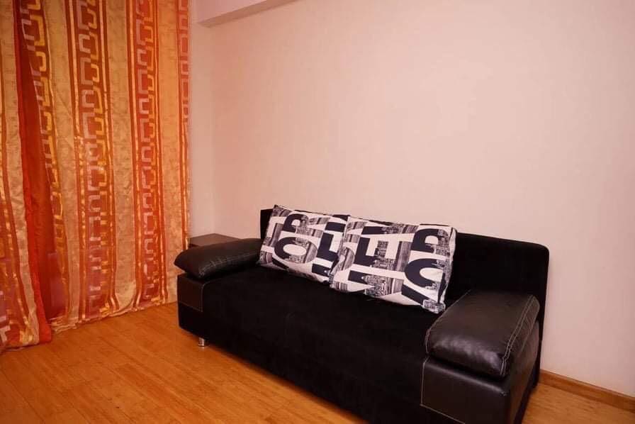 Living room with a black sofa and bright curtains in an apartment for sale in Budva, Montenegro. Bright interior with laminate flooring.