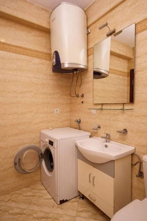 Bathroom in an apartment in Budva, Montenegro: beige tiles, washing machine, water heater, and vanity with sink.