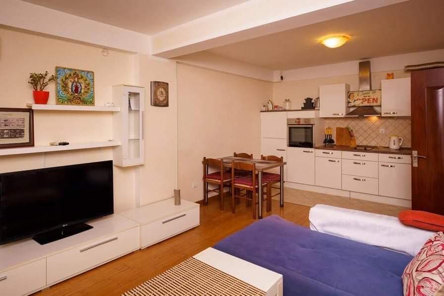Living room with kitchen in an apartment in Budva, Montenegro: light-colored furniture, dining area, TV area, and sofa in the interior.