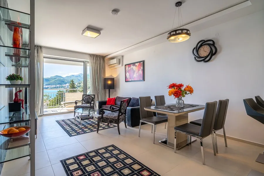 Living room with sofa, dining table, and balcony door overlooking the sea and mountains.