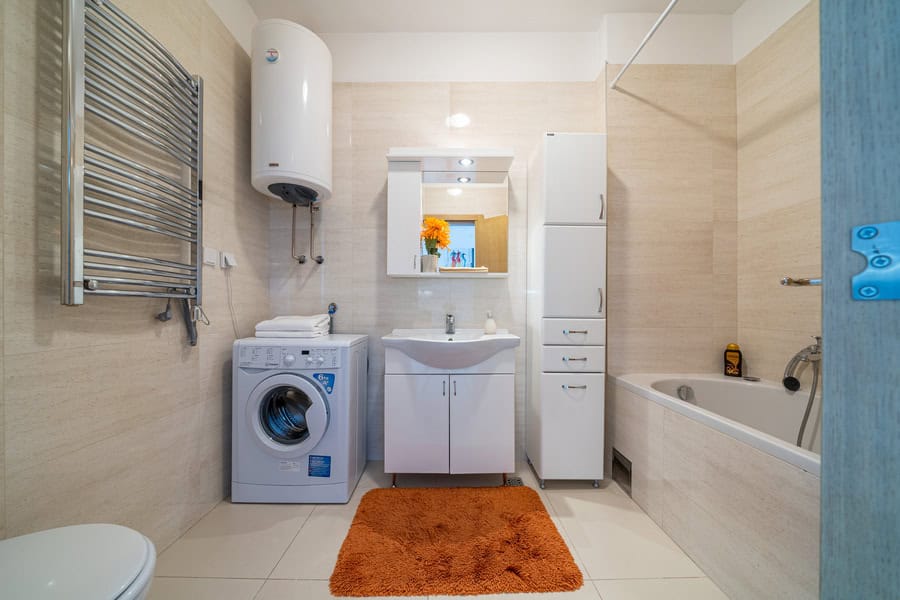 Bathroom featuring a sink, bathtub, washing machine, water heater, and heated towel rail.
