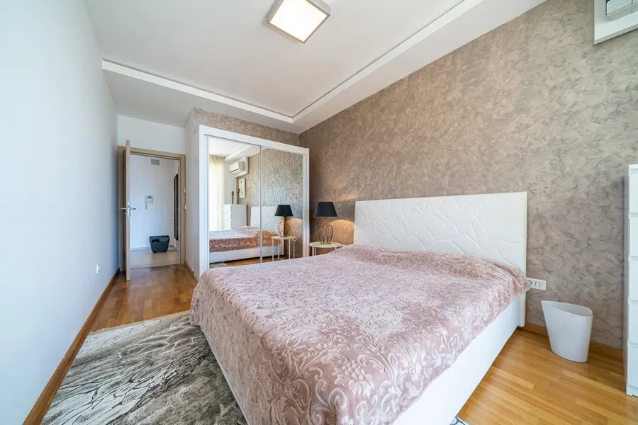 Bedroom featuring a white bed with pink cover, mirrored wardrobe, and wooden flooring.