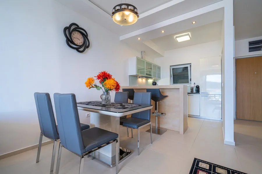 Dining area with blue chairs and a kitchen bar counter visible in the background.