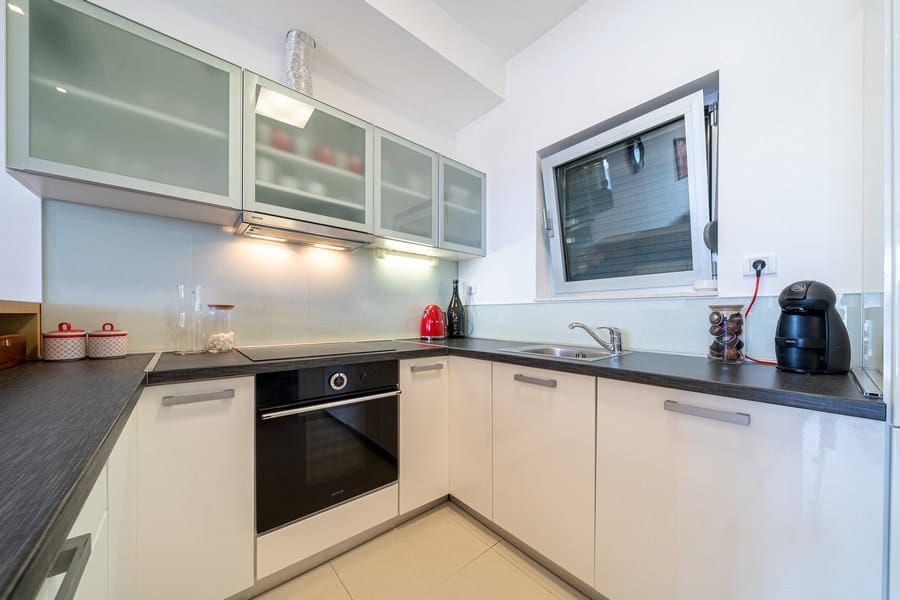 Modern kitchen with white cabinets, black countertop, built-in oven, sink, and coffee maker visible.