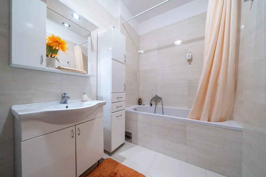 Modern bathroom featuring a white vanity sink, mirrored cabinet, bathtub with a peach curtain, and light tiled walls.