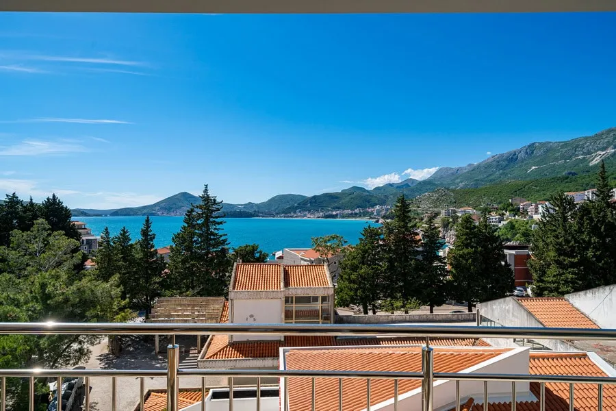 View from a balcony with metal railing overlooking the sea and mountains.