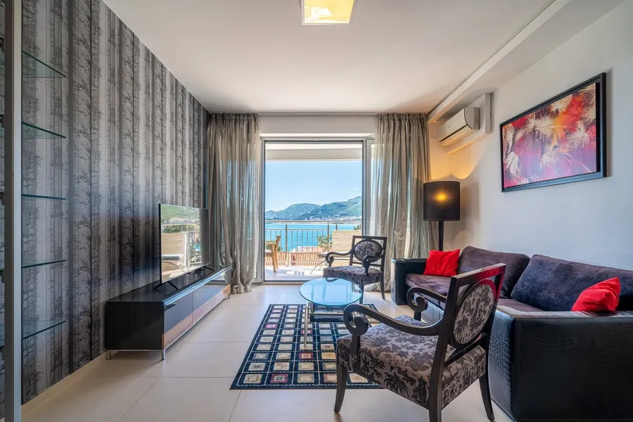 Living room with sofa, armchairs, TV, coffee table, and a view of the sea through glass doors.