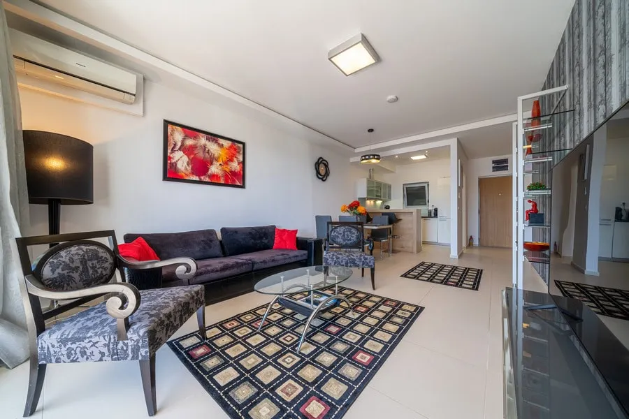 Living room featuring a dark sofa, patterned armchairs, glass coffee table, and wall art.