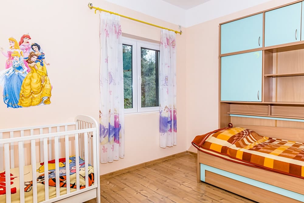Children's bedroom in an apartment in Đenovići, Montenegro: crib, single bed, wardrobe, and princess-themed decor.