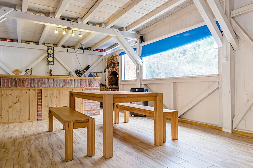 Wooden hall with beams, brick oven, and wooden table with benches on laminate flooring.
