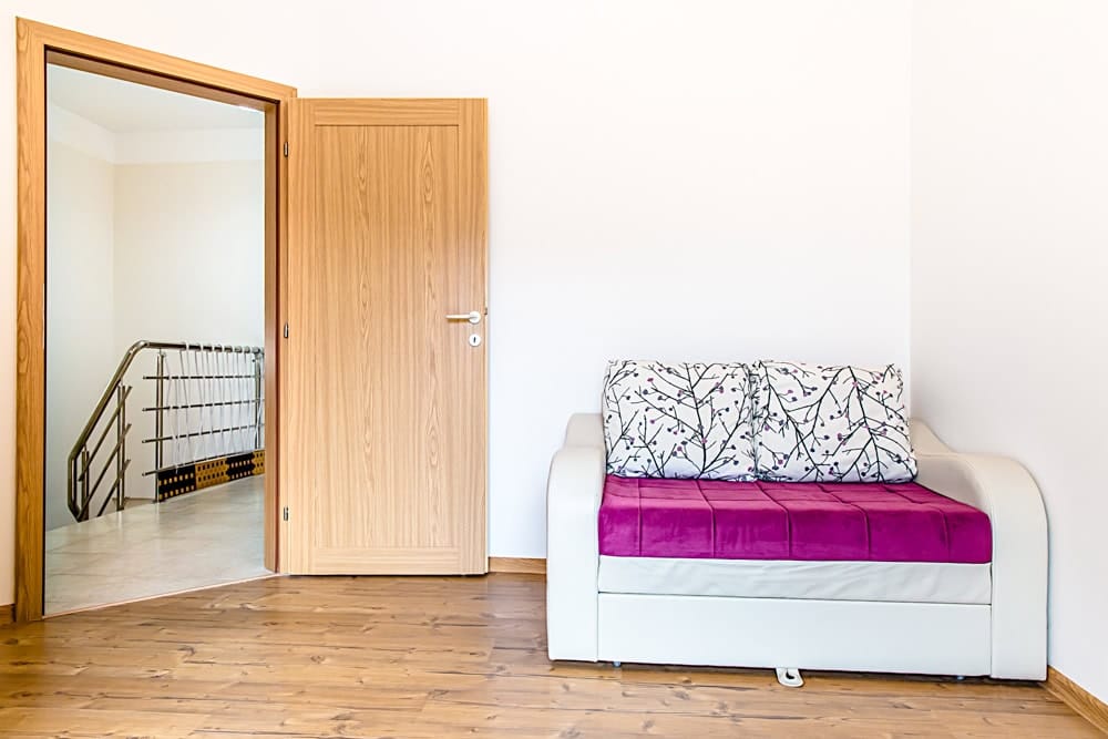 Living room with a bright sofa and a wooden door in an apartment in Đenovići, Montenegro. Bright interior with laminate flooring.