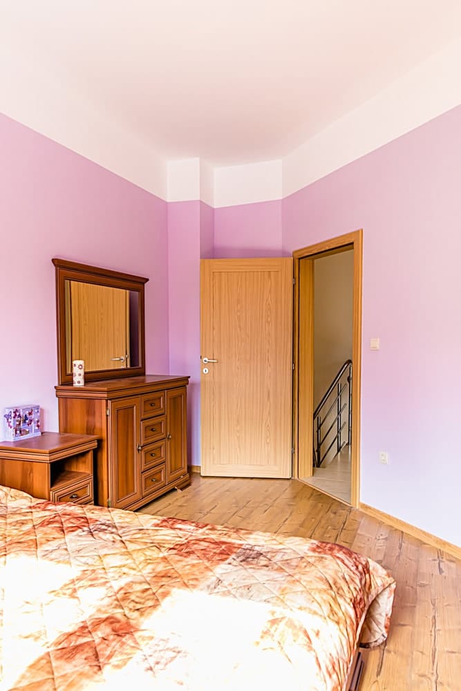 Bedroom in an apartment in Đenovići, Montenegro: wooden furniture, a dresser with a mirror, light walls, and a view of the staircase.