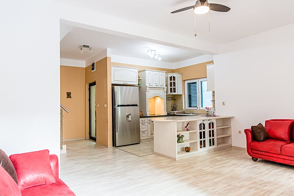 Living room with kitchen in an apartment in Đenovići, Montenegro: light furniture, a red sofa, and modern appliances.