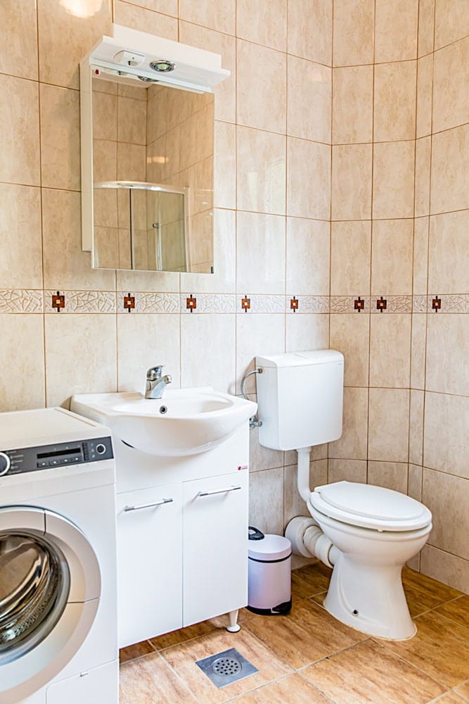 Bathroom in an apartment in Đenovići, Montenegro: light tiles, vanity with sink, mirror, and washing machine.