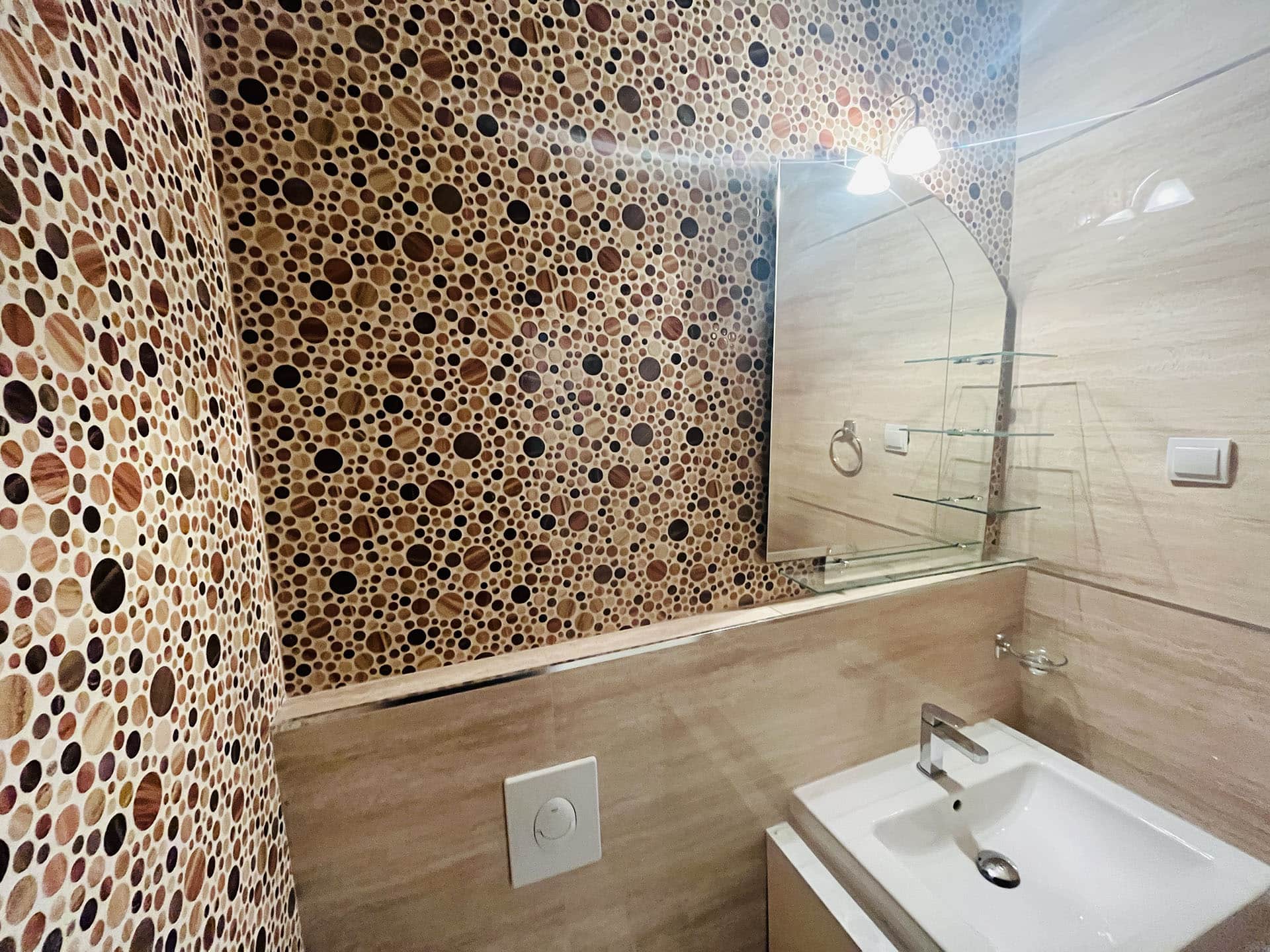 Modern bathroom in an apartment in Budva, Montenegro: mosaic tiles, mirror, and light-colored fixtures.