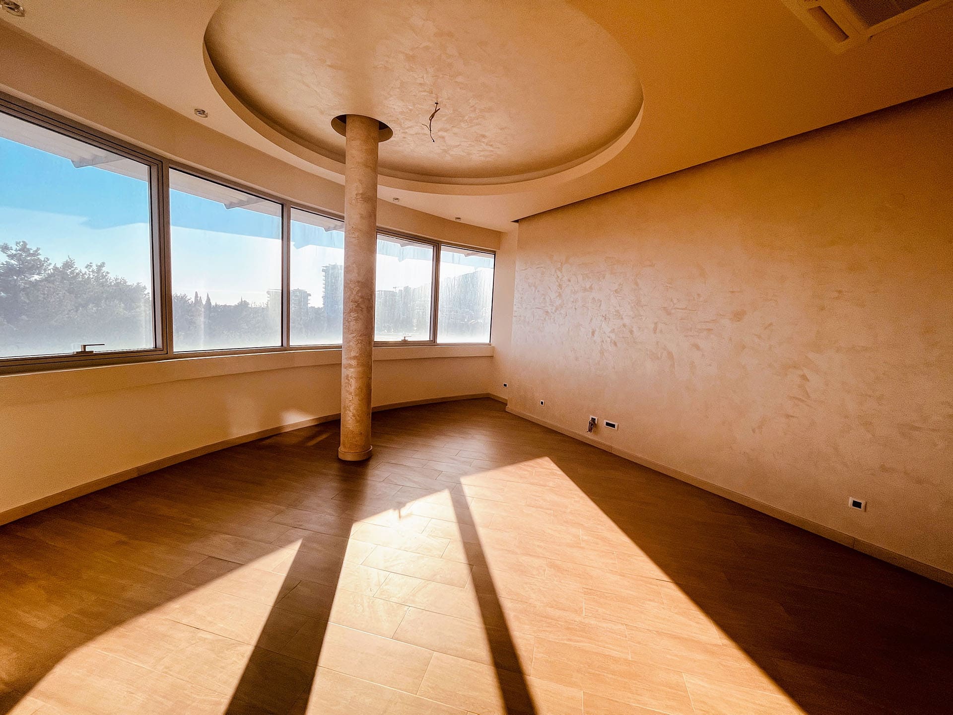 Bright living room in an apartment in Budva, Montenegro: panoramic windows, a decorative column, and loft-style wall finishes.