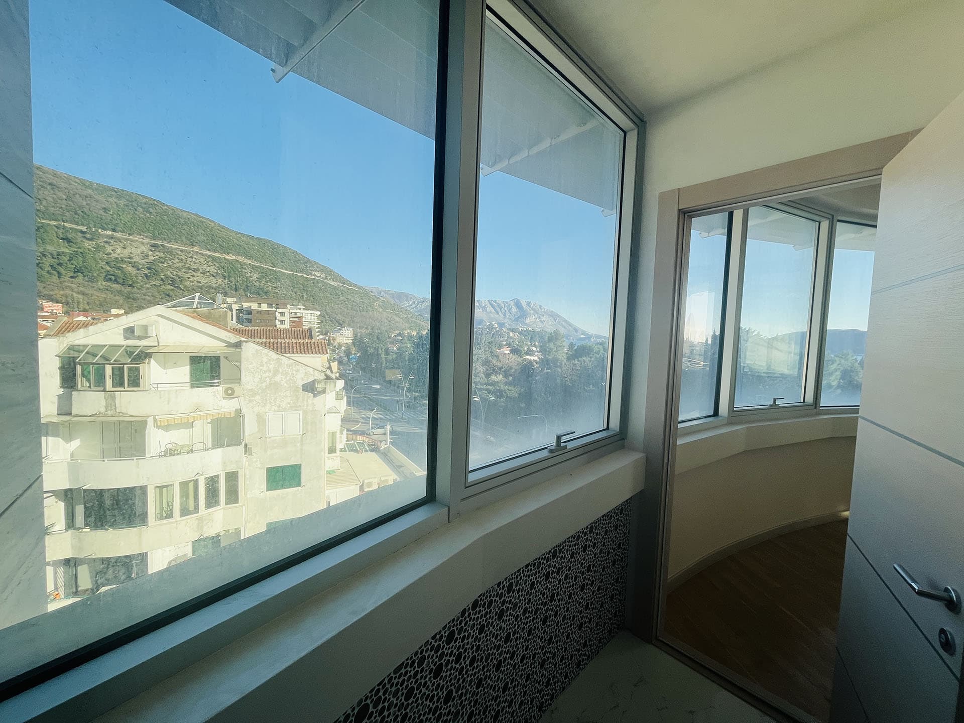 Panoramic view of the mountains and city from the glazed balcony of an apartment in Budva, Montenegro, with modern finishes.