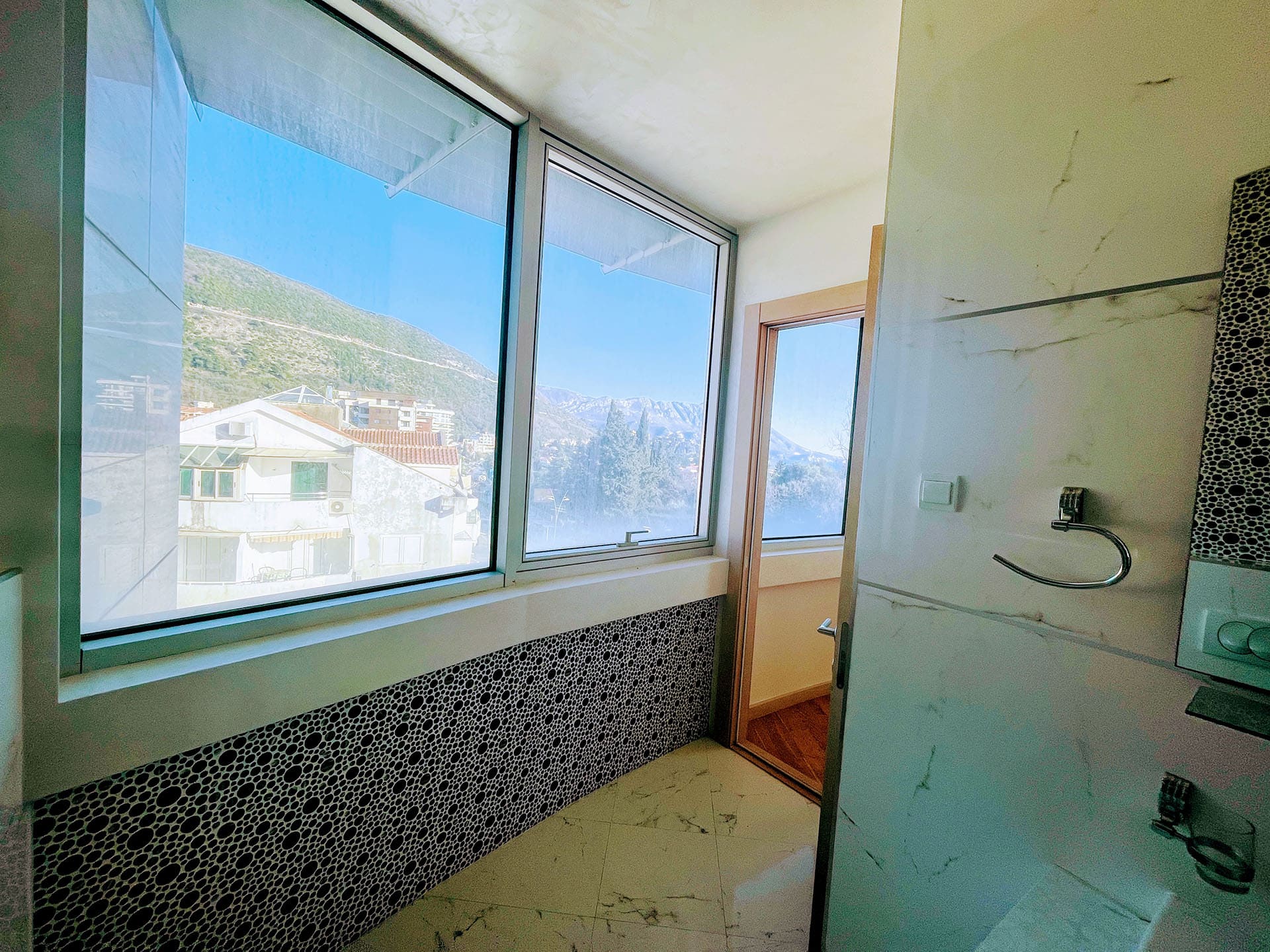 Bathroom with a panoramic window and mountain view in an apartment in Budva, Montenegro: modern tile and finishes.