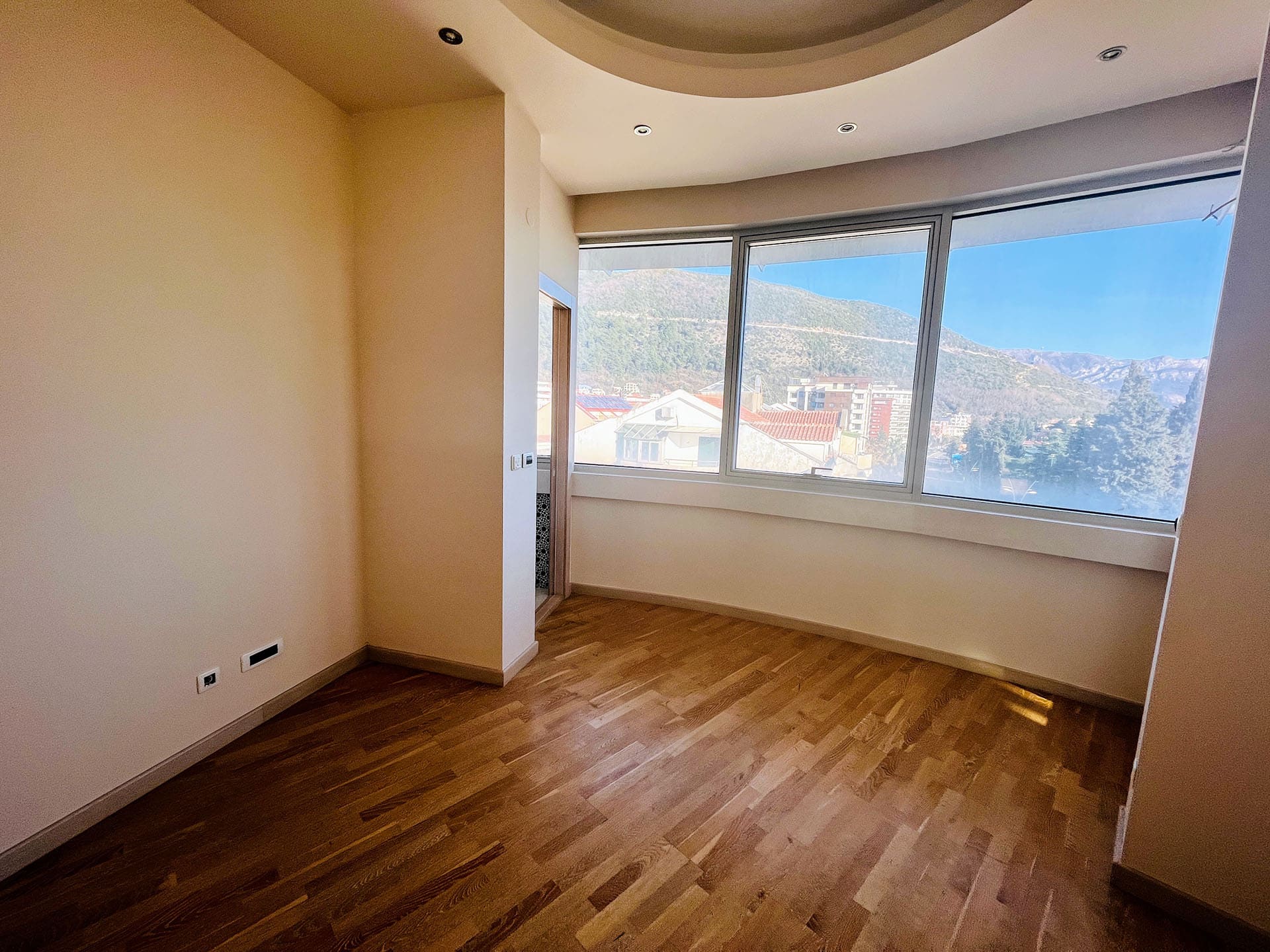 Bright living room with panoramic windows and mountain views in an apartment, Budva, Montenegro, parquet flooring, recessed lighting.