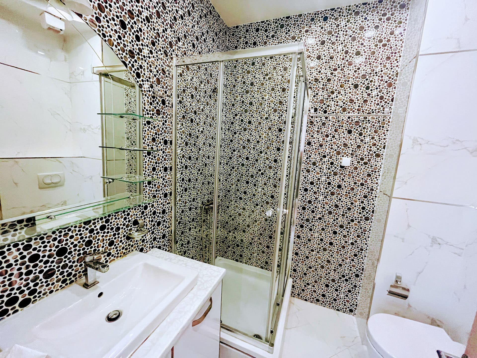 Modern bathroom in an apartment in Budva, Montenegro: shower cabin, stylish mosaic tile, and white sanitary ware.