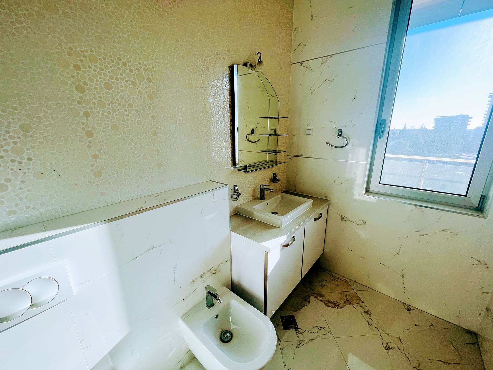 Modern bathroom with bidet and window in an apartment in Budva, Montenegro: marble-look tile finish and mirror.