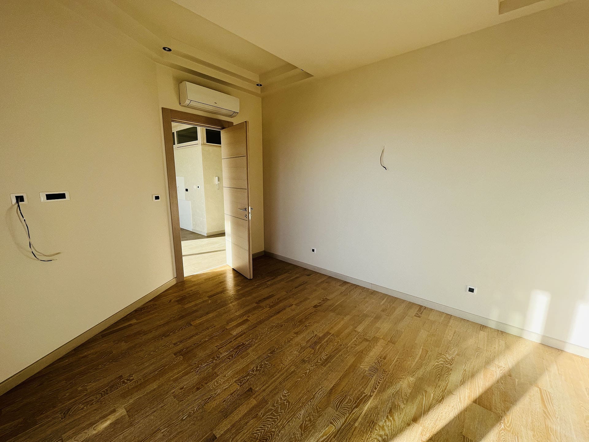 Bright bedroom with parquet flooring and air conditioning in a new apartment in Budva, Montenegro. Empty room with finishing.
