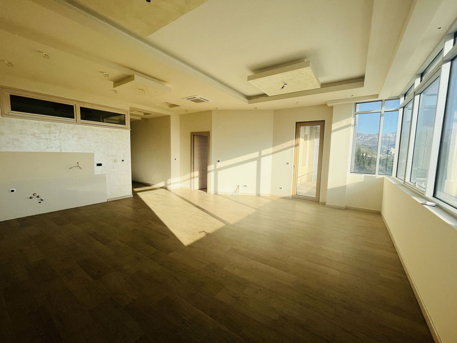 Spacious living room in a new apartment in Budva, Montenegro: panoramic windows, light finishes, and wooden flooring.