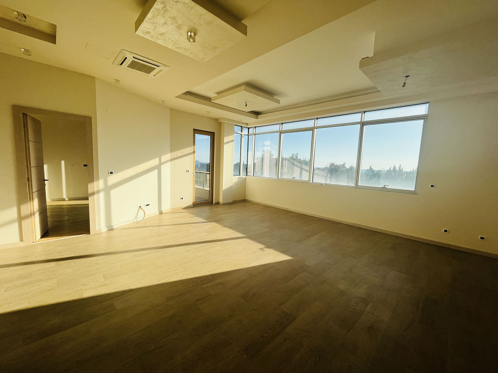 Spacious living room in a new apartment in Budva, Montenegro: panoramic windows, bright interior, and access to the balcony.