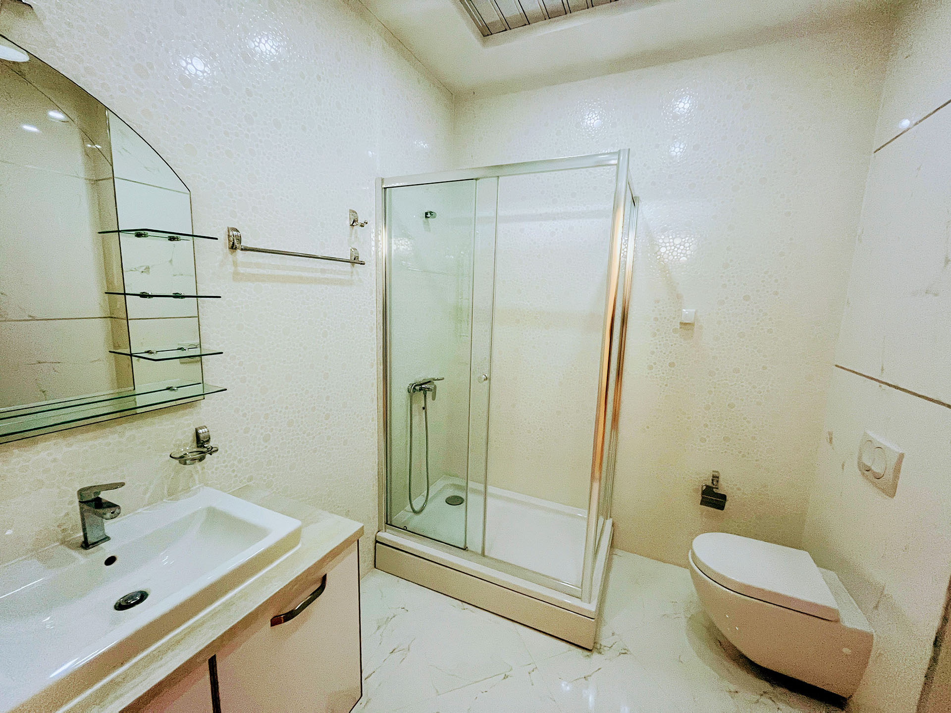 Modern bathroom in an apartment in Budva, Montenegro: shower cabin, wall-mounted toilet, and vanity with sink.