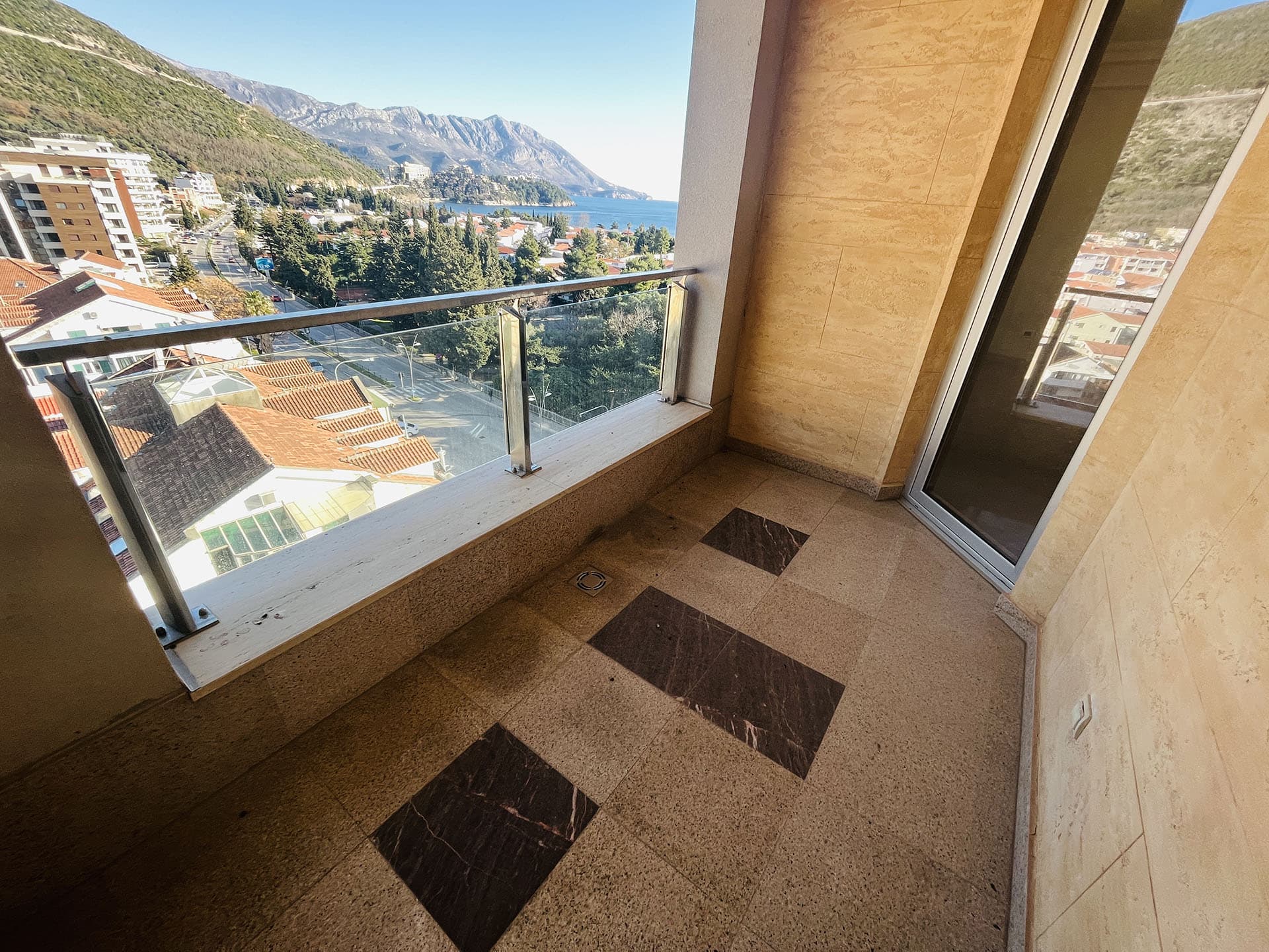 Balcony in an apartment in Budva, Montenegro: panoramic view of the sea, mountains, and city, stone finish, glass railing.